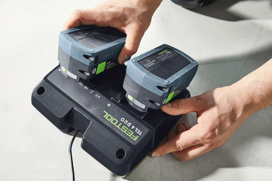 Festool TCL 6 DUO Schnellladegerät mit zwei Li-Ionen Akkupacks in Ladeschächten, von Hand gehalten.