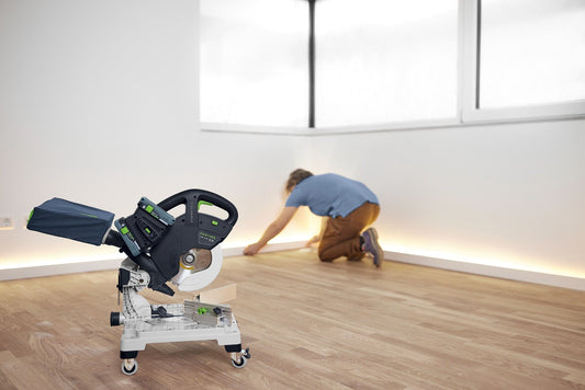 Festool SYMC 70 EB Akku-Leistensäge mit Rollen auf Baustelle, im Hintergrund Handwerker beim Leistenschnitt